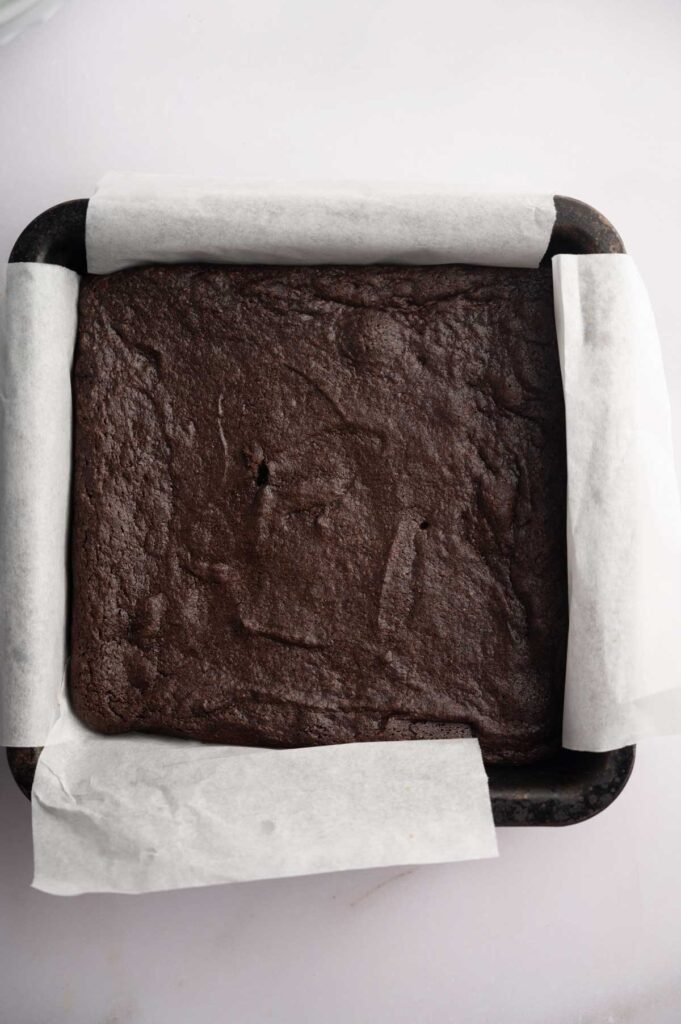 A square pan lined with parchment paper holds baked Mint Chocolate Brownies, featuring a smooth, slightly cracked surface.