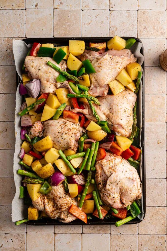 Sheet Pan Chicken Thighs and Veggies arranged on parchment paper with diced potatoes, asparagus, red onion, and bell peppers&mdash;all ready for roasting.