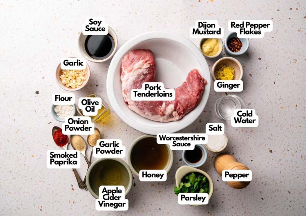 Raw pork tenderloins in a bowl surrounded by labeled small bowls of various ingredients and seasonings on a speckled countertop—perfect for preparing Slow Cooker Pork Tenderloin.