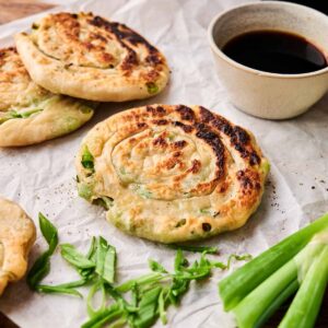 Three Air Fryer Scallion Pancakes on parchment paper, garnished with chopped green onions, served beside a small bowl of soy sauce.