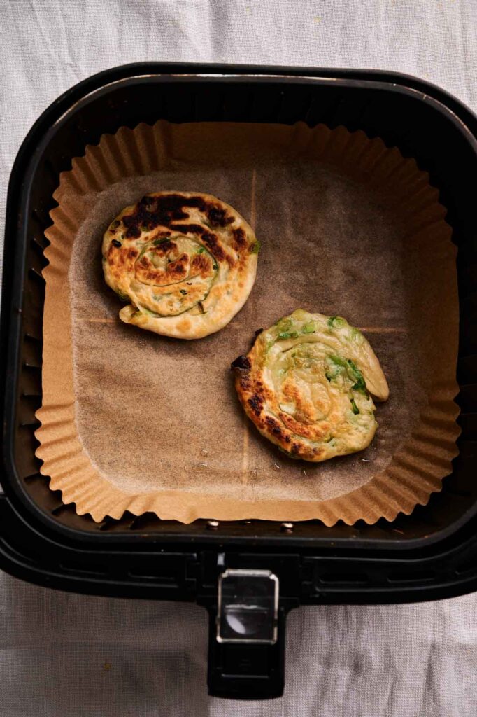 Air Fryer Scallion Pancakes sit perfectly cooked on parchment paper inside the air fryer basket, ready to enjoy.