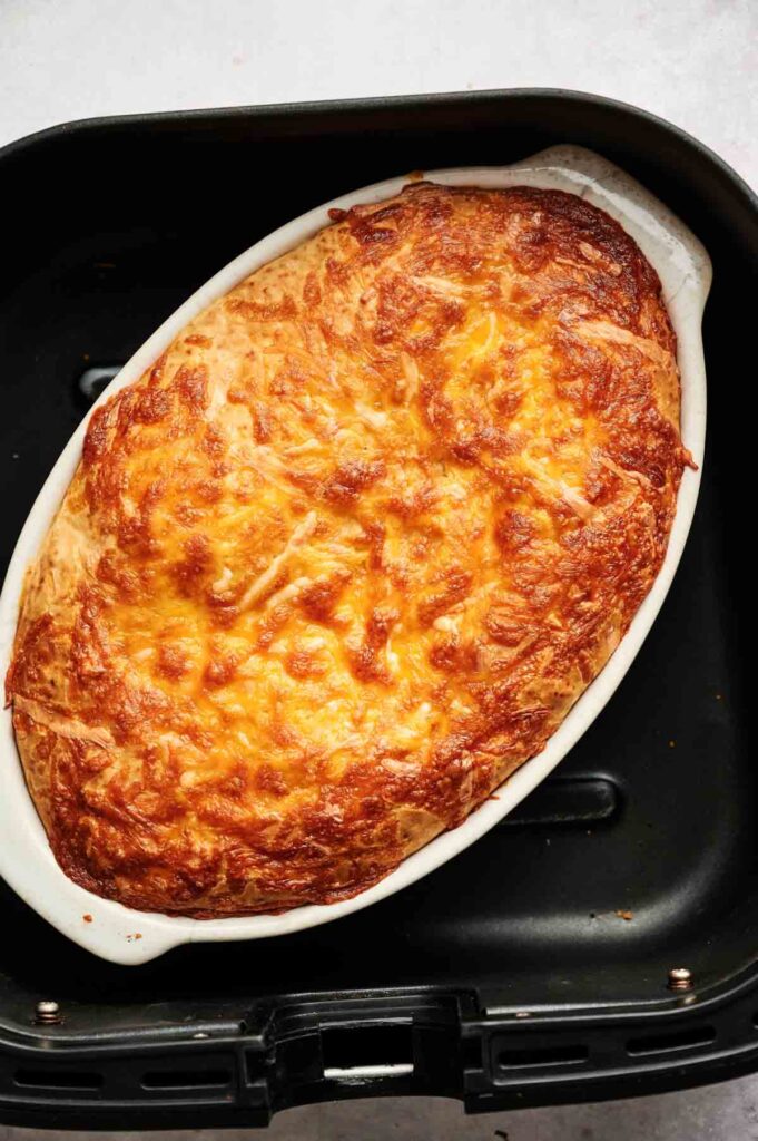 A baked Air Fryer Sloppy Joe Casserole with a golden, melted cheese topping sits in a white oval dish inside a black air fryer basket.