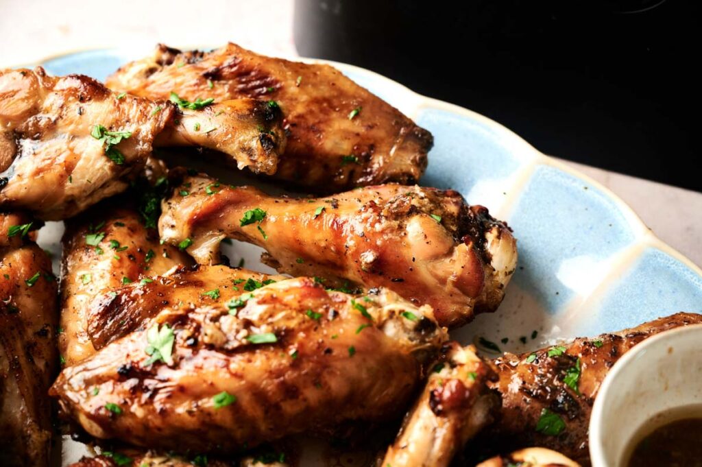 A plate of air fryer turkey wings garnished with chopped herbs, with a small bowl of sauce visible at the edge.