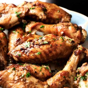 A plate of crispy air fryer turkey wings garnished with chopped herbs, displayed on a light-colored dish.