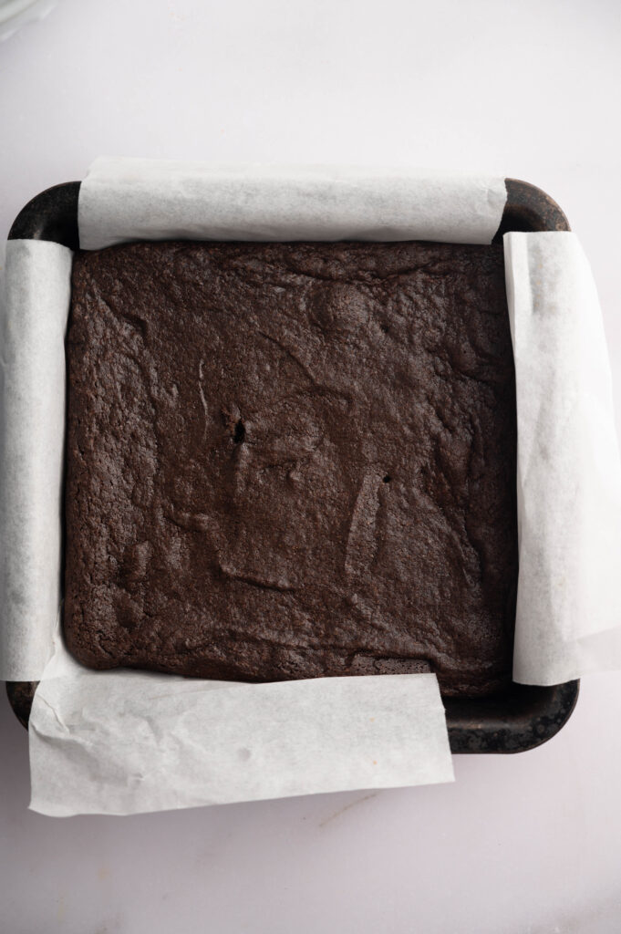 A square baking tray lined with parchment paper holds a freshly baked slab of Air Fryer Mint Chocolate Brownies on a light surface.