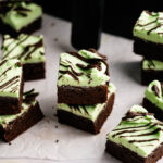 Air Fryer Mint Chocolate Brownies: Brownie squares topped with green mint frosting and chocolate drizzle, arranged on parchment paper.