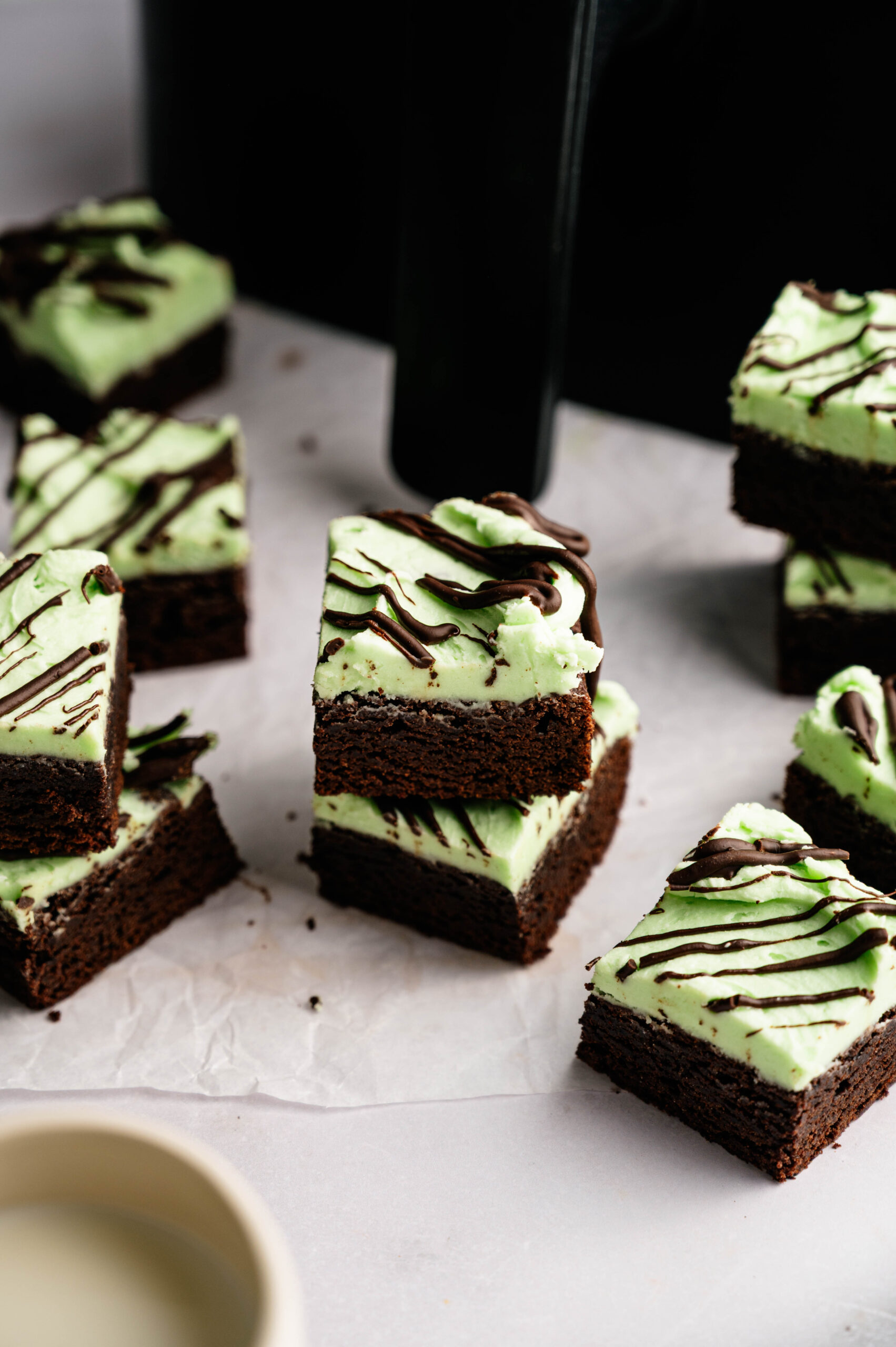Air Fryer Mint Chocolate Brownies: Brownie squares topped with green mint frosting and chocolate drizzle, arranged on parchment paper.