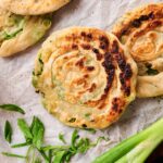 Two cooked Air Fryer Scallion Pancakes on parchment paper, garnished with sliced green onions and a raw scallion nearby.