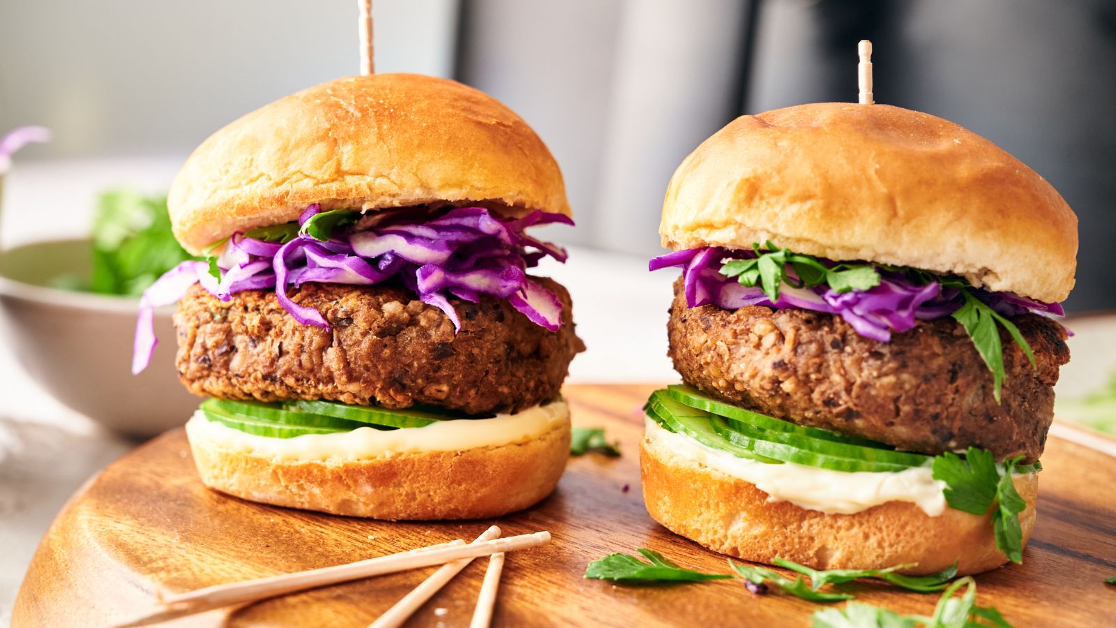 Two veggie burgers with lettuce, cucumber slices, purple cabbage, and mayonnaise in buns, placed on a wooden board.