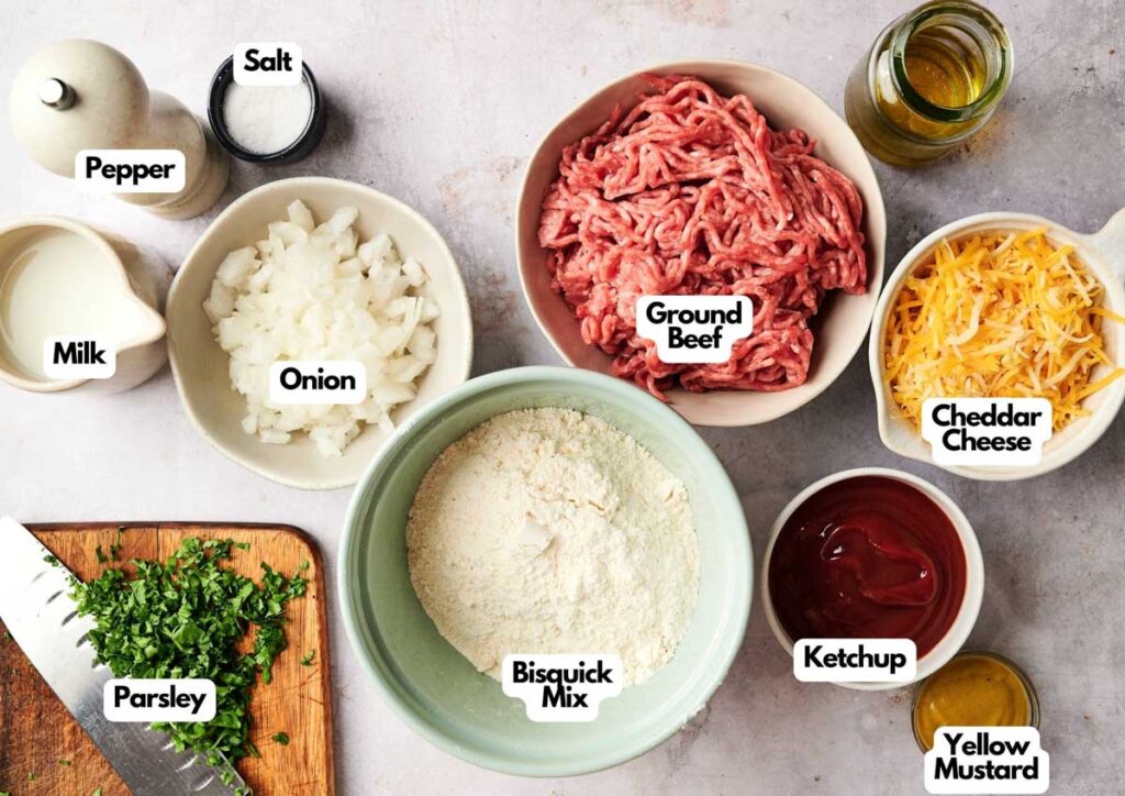 Top-down view of labeled ingredients for Air Fryer Sloppy Joe Casserole in bowls: ground beef, cheddar cheese, onion, ketchup, Bisquick mix, parsley, milk, yellow mustard, salt, pepper, and a bottle of oil.