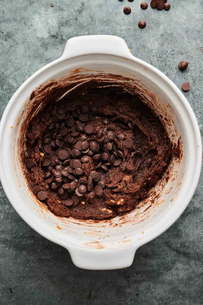 A white mixing bowl filled with chocolate cookie dough and chocolate chips, perfect for making Air Fryer Sweet Potato Brownies, sits on a gray countertop.