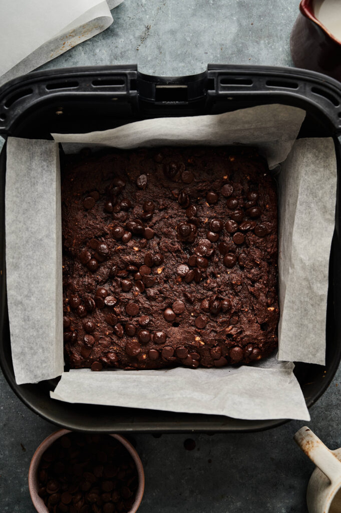 A square pan lined with parchment paper holds the Air Fryer Sweet Potato Brownies, topped generously with chocolate chips.
