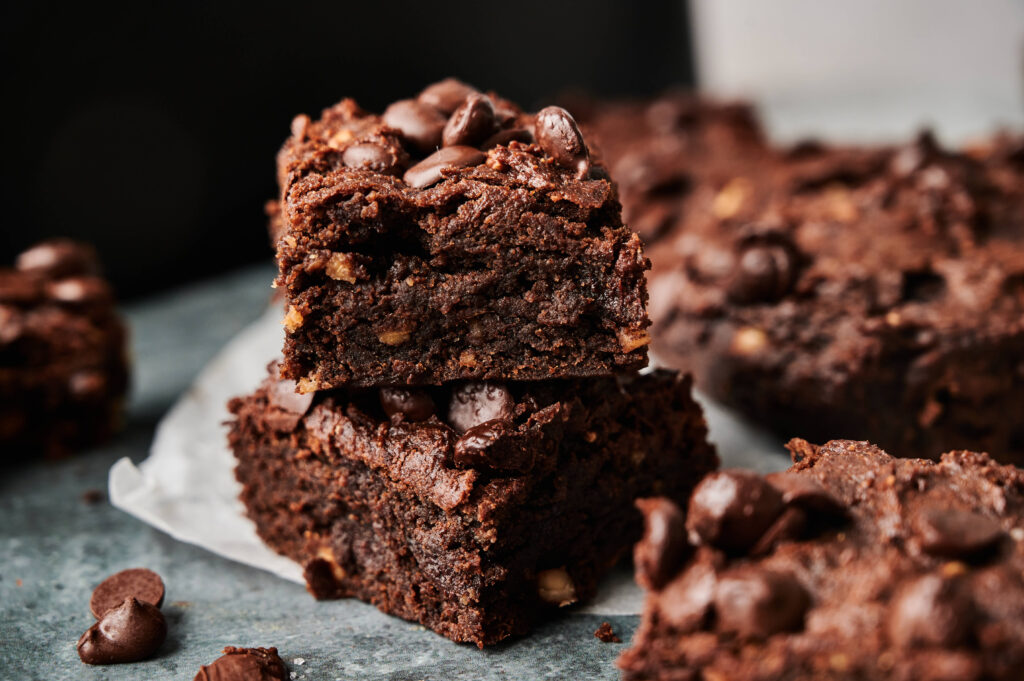 Two sweet potato brownies stacked on top of each other, topped with chocolate chips, with more Air Fryer Sweet Potato Brownies in the background.