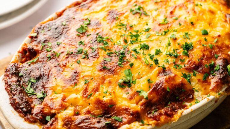 A baked casserole topped with melted, browned cheese and garnished with chopped fresh parsley in a white dish.