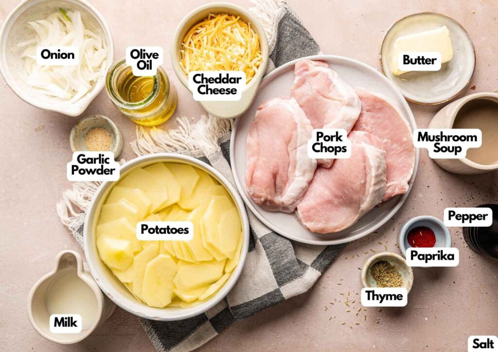 A flat lay of raw pork chops, sliced potatoes, grated cheddar, onion, olive oil, butter, milk, mushroom soup, and seasonings labeled with text&mdash;perfect ingredients for a classic Pork Chop Casserole.