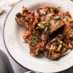 A plate of Air Fryer Lamb Loin Chops garnished with garlic and rosemary, served on a white dish with a black rim.