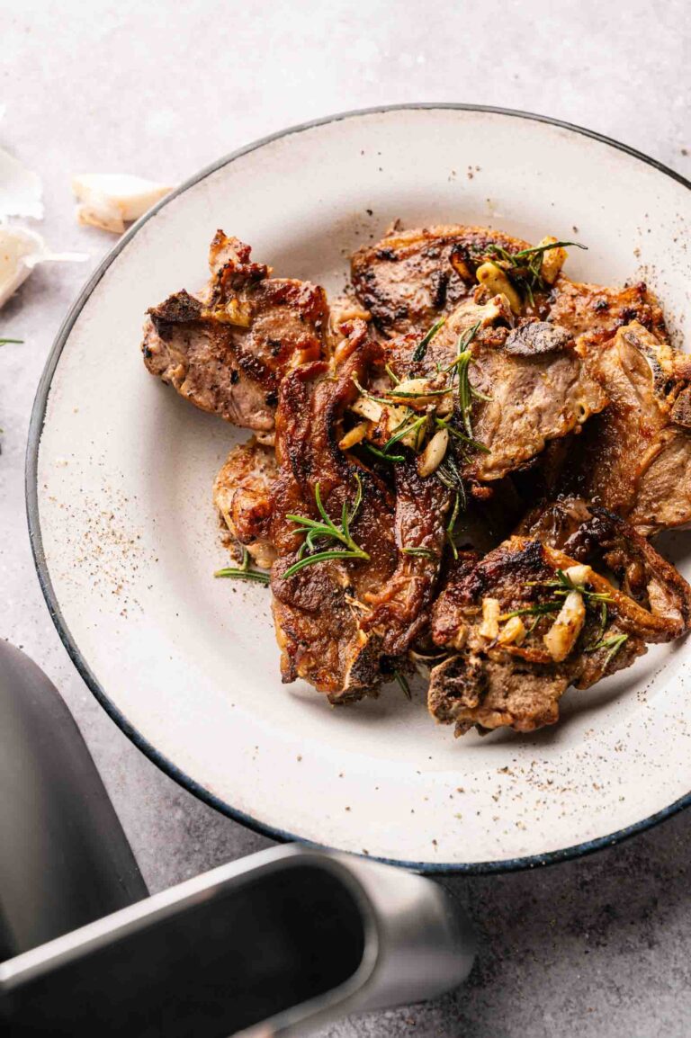 A plate of Air Fryer Lamb Loin Chops garnished with garlic and rosemary, served on a white dish with a black rim.