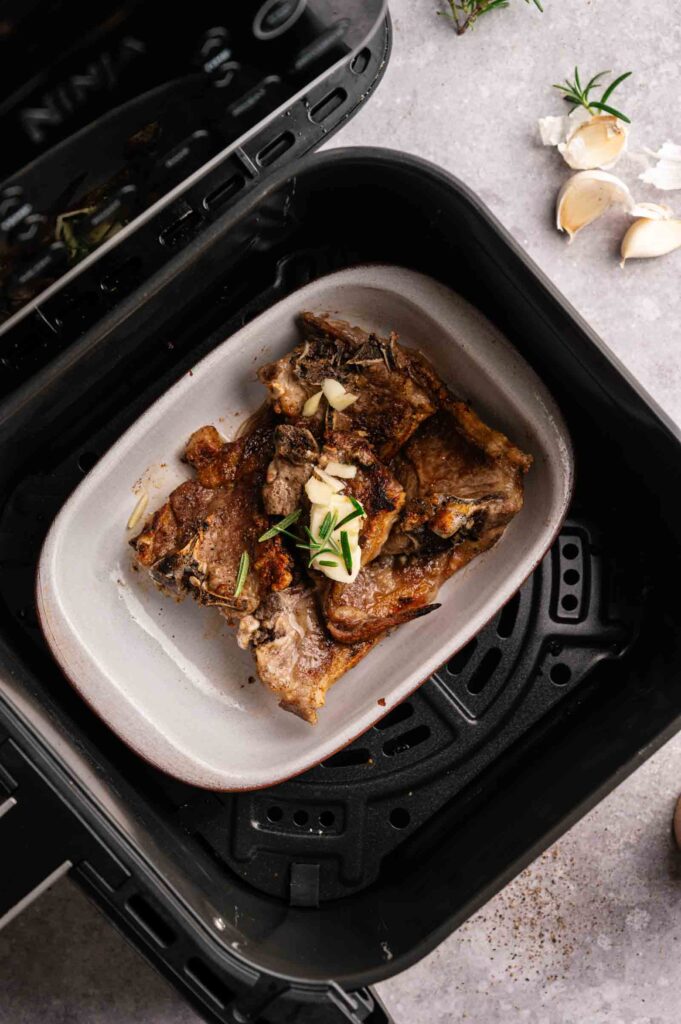 Air Fryer Lamb Loin Chops garnished with rosemary and sliced garlic in a small tray inside an air fryer.