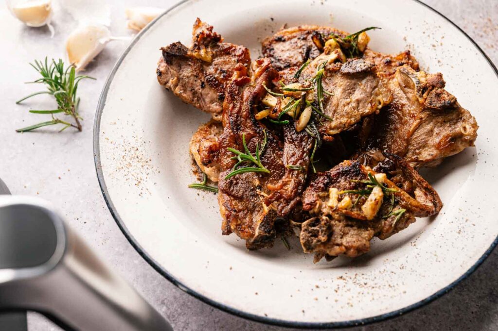 A plate of Air Fryer Lamb Loin Chops garnished with rosemary and sliced garlic, served on a white dish.