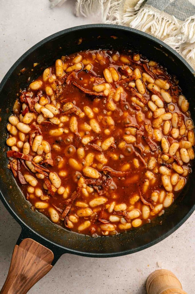 A skillet filled with Baked Beans in a tangy tomato-based sauce, mixed with sun-dried tomatoes and savory seasonings.