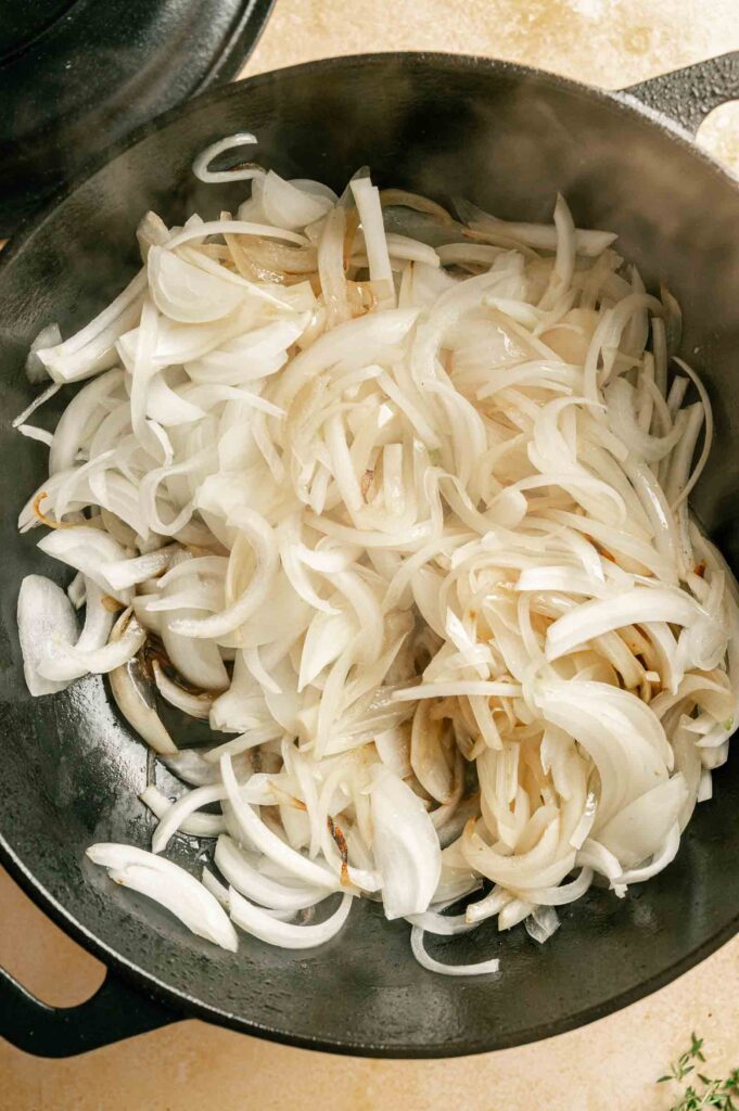 Sliced onions cooking and starting to caramelize in a black skillet—the perfect base for a savory French Onion Pot Roast.