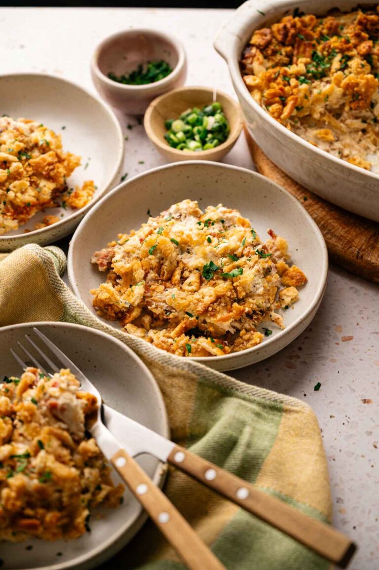 Three bowls of Air Fryer Neiman Marcus Chicken Casserole topped with crispy crumbs, served with forks, alongside a casserole dish and small bowls of chopped green onions and parsley.