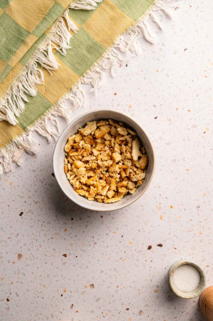 A bowl of crumbled Ritz crackers sits on a speckled countertop next to a small container, with a fringed green and yellow cloth nearby&mdash;perfect for pairing with Air Fryer Neiman Marcus Chicken Casserole.